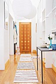 Narrow hallway with white, paper pendant lamps above rugs on wooden floor and wooden front door at far end