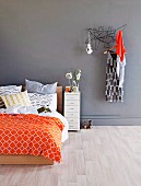 Double bed with modern, colourful bed linen next to dress hanging on clothes rack on grey wall