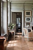 Blick durch offene Zimmertüren eines herrschaftlichen Salons mit antikem Beistelltisch am Fenster und zierlichem Sessel auf Fischgrätparkett
