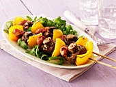 Kebabs with yellow peppers, mushrooms and meat on a bed of rocket on an oval plate