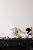 weiße Dekoobjekte wie griechische Büste, Muschelgehäuse und Vasen auf Ablage aus schwarzem Marmor