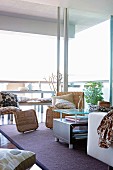 Seating area with modern wicker chairs and coffee table in front of floor-to-ceiling sliding windows; simple dining area on terrace in background