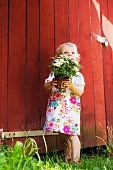 Little girl hold a potted plant in front of a shed