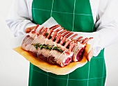 A man holding a fresh rack of lamb with rosemary