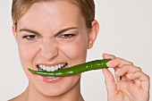 Junge Frau hält eine grüne Chilischote zwischen den Zähnen