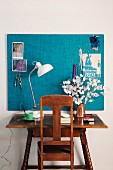 Dark wood, vintage desk and chair below pinboard with turquoise fabric cover