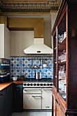 Blue and white wall tiles between gas cooker and extractor hood in old wooden kitchen with neoclassical stucco ceiling