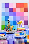 Figurine, books and pots of paint in front of colour sampler on wall
