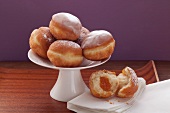 Several doughnuts on a cake stand, and one doughnut, broken open, on a white napkin