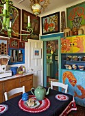 Artistically inspired kitchen decor with naïve, South African paintings on walls and tablecloth with ethnic pattern
