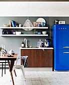 weiße Regale über Spültisch in Holzoptik, daneben leuchtend blaue Kühlschrank