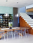 Plexiglass chairs at massive wooden table; wine rack and open-plan staircase without bannister in background