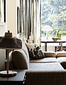 Comfortable sofa and side table with table lamp in front of window with view of garden