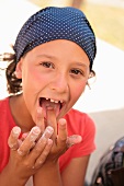 A girl wearing a bandanna licking her fingers