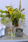 Posy in wine glass behind perfume bottle and crystal jar with metal lid