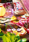 Colourful blankets, flip-flops, teacup and cushions on garden bench with flower-shaped floating candles in foreground