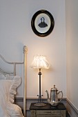 Oval portrait above nostalgic bedside lamp and silver coffee pot on bedside table