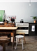 Rustikaler Küchentisch und Hocker vor improvisierter Küchenzeile in karger Küche