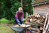 Junge Frau füllt eine Schubkarre mit gehacktem Brennholz