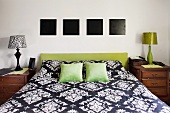 Doppelbett mit gepolstertem Kopfende in Olivgrün; darüber vier quadratische, monochrome Bilder in Schwarz