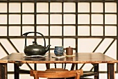 Ceramic teapot and teacups on Chinese-style wooden table: geometric wooden wall decoration in background