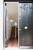 Blick durch offene Haustür aus dunklem Holz und schmiedeeisernem Beschlag in modernes Treppenhaus