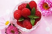 Fresh raspberries in a glass bowl surrounded by pink flowers
