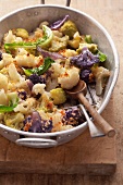 White and purple cauliflower with breadcrumbs in a baking tin on a wooden board