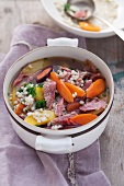 Mixed stew with meat, vegetables and barley in a white pot