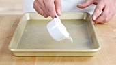 A baking tray being sprayed with a non-stick spay and dusted with flour