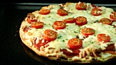 A pizza topped with mozzarella and cherry tomatoes baking in the oven