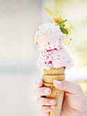 A hand holding a cone with strawberry ice cream