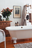 Traditionelles Badezimmer mit freistehender Badewanne, einer Vintage-Kommode und einem prachtvollen Rosenstrauss in einer Glasvase