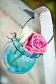 Two roses in blue glass sphere with wire handle hanging from back of chair
