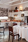 Country-house-style kitchen with antique leather chairs around set table with white tablecloth