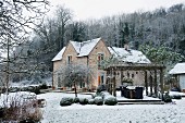 Wintery garden with seating area below climber-covered pergola and box balls in front of caretaker's house belonging to English hunting lodge