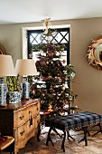 Ottoman upholstered in tartan with antler legs in front of decorated Christmas tree and antique chest of drawers in English living room