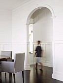 Tall, arched doorway connecting elegant rooms with white wall panelling and exotic wood parquet floor