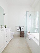 Hohes Badezimmer im eleganten weißen Landhausstil mit Duschabtrennung aus Glas und naturfarbenen Fliesen am Boden