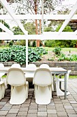 Terrace table with panton chairs under a bare, white pergola