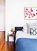 Bed with blue bedspread next to simple wooden bedside table