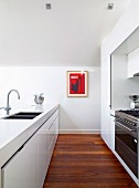 View along open-plan designer kitchen with glossy white fronts, parquet floor and picture on wall