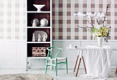 Checkered wallpaper in natural colors; in front of it a white crockery shelf with a brown inner surface and a white table with an elegant bouquet of spring flowers