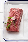A fillet steak with tarragon and garlic on parchment paper in a roasting tin