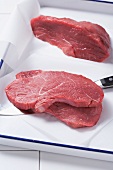 Steaks on baking paper in a roasting tin with a knife