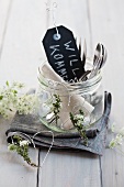 Welcome sign and cutlery in preserving jar next to hearts made from wire and herbs