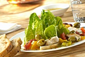 A salad with pepper, chicken breast and green olives