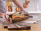 A man holding crispy roast pork in a roasting tin