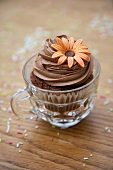 A chocolate cupcake decorated with a marzipan flower in a glass cup