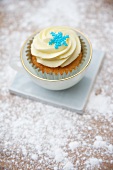 A cupcake decorated with light frosting and a sugar snowflake in a cup